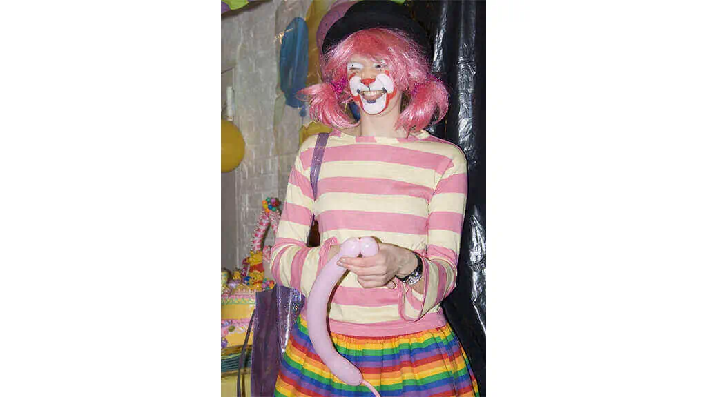 Female balloon artist in a clown costume making a balloon animal at a kids party