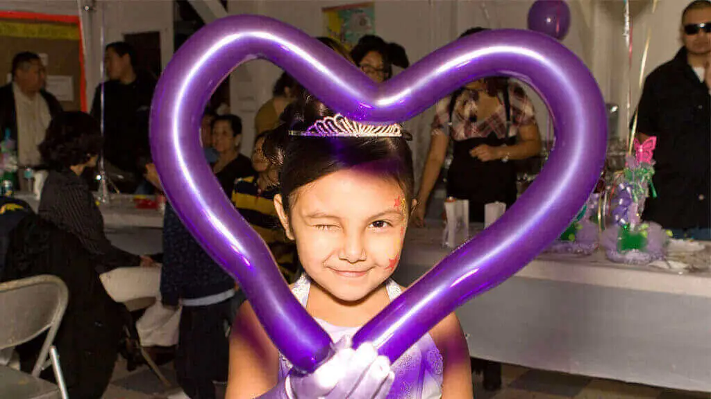 Girl at a birthday party holding a purple twisted balloon heart made by our balloon artist