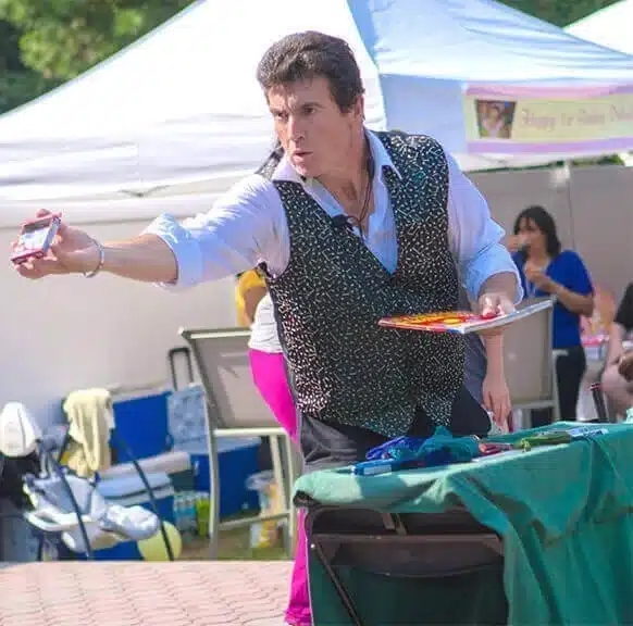 Children's magician performing a trick under a party tent