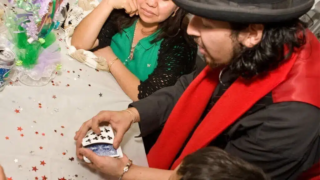 Magician in a black hat shuffling cards at a party table