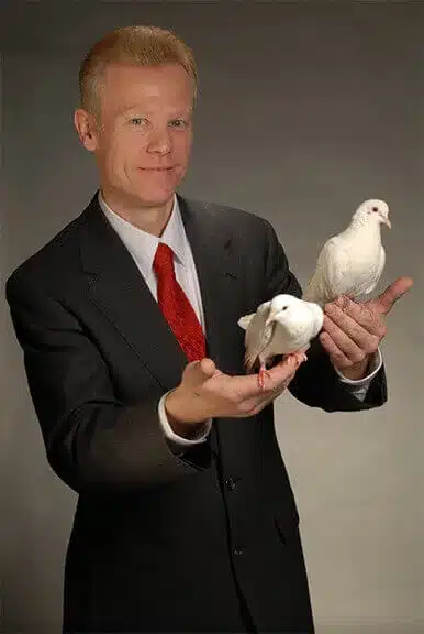 Magician in a suit holding two white doves