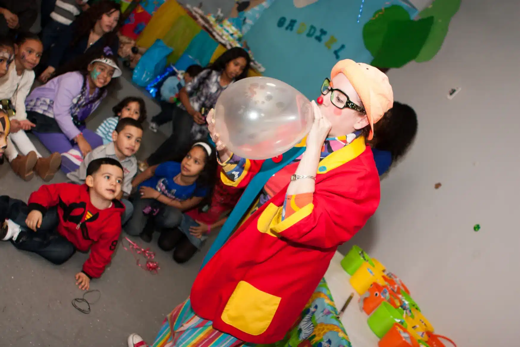 Birthday clown blowing up a giant balloon while kids sit on the floor