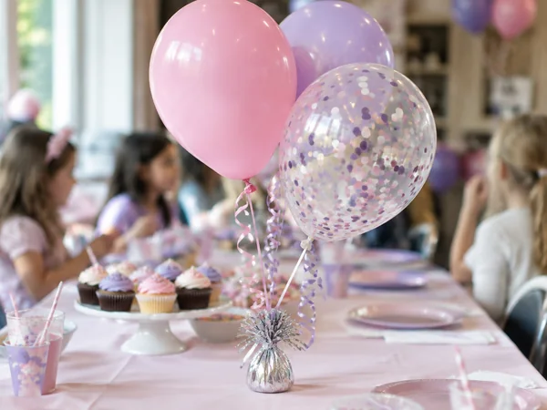 Balloon centerpiece of pink, lilac and confetti helium balloons on a birthday table
