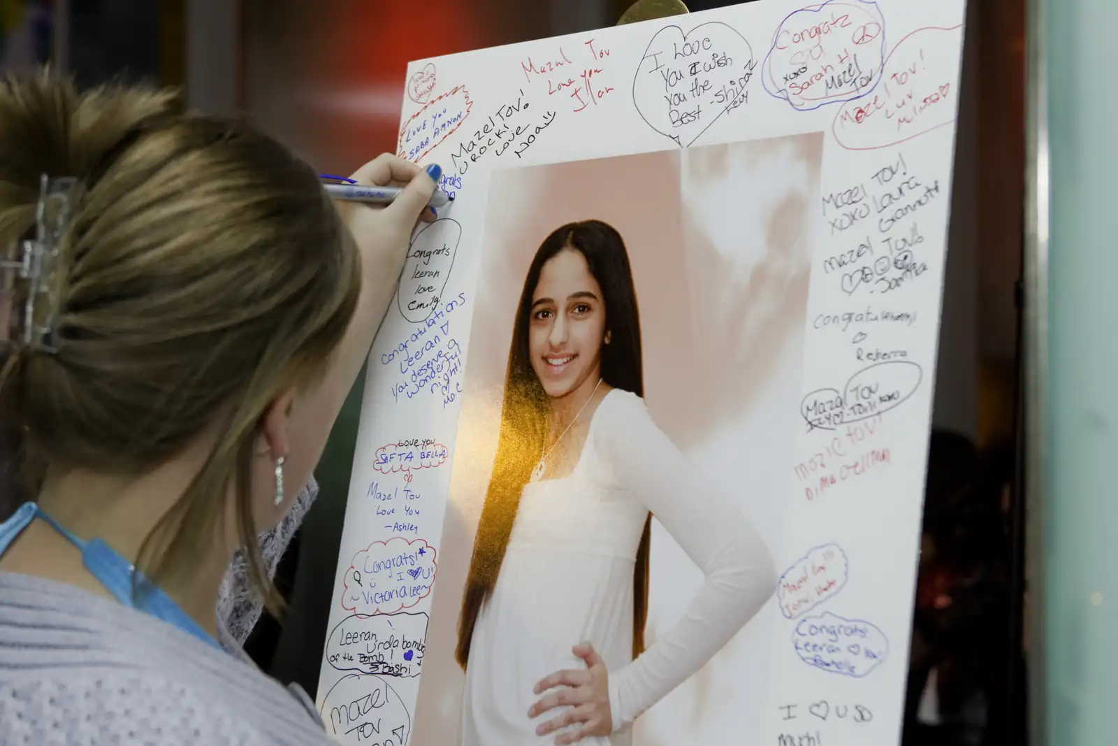 Guest writing a message on a bat mitzvah sign-in board with a portrait of the girl