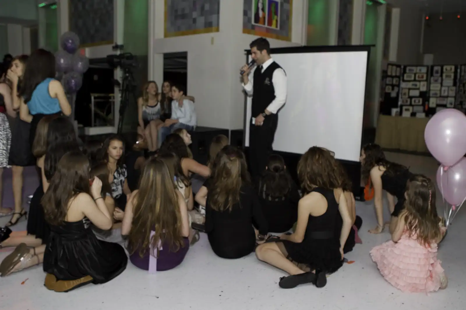 MC leading games for kids seated on the dance floor, with a projector screen at a bat mitzvah