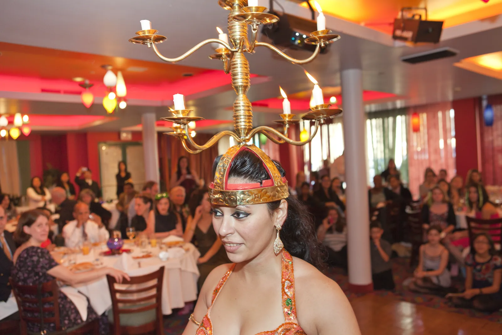 Belly dancer balancing a lit candelabra on her head at a restaurant party