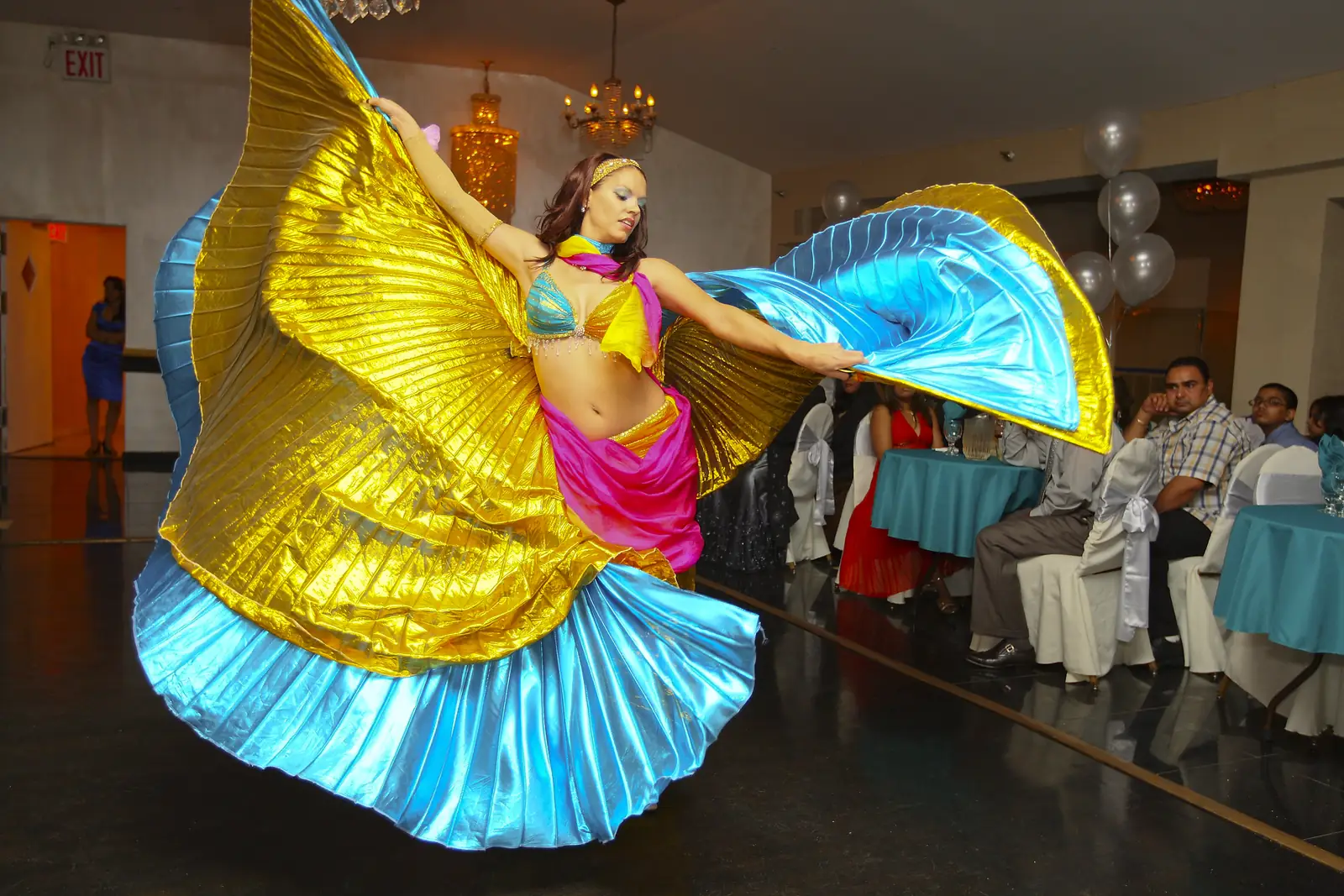 Belly dancer spinning gold and blue Isis wings in a party hall