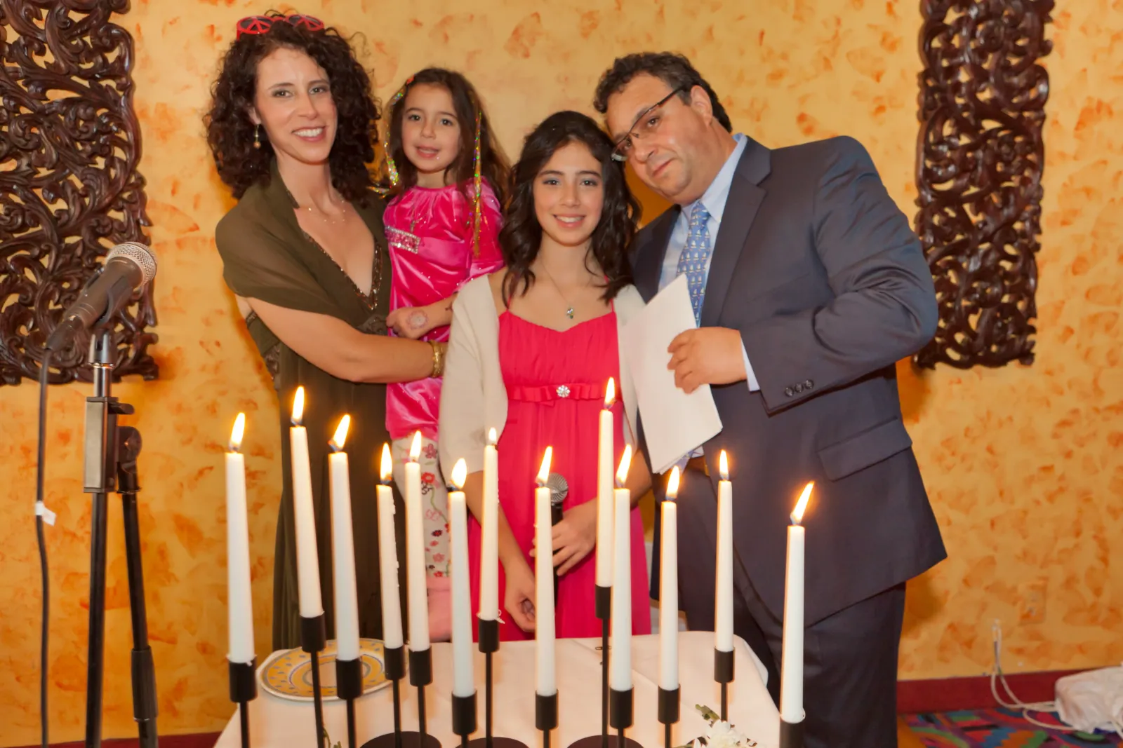 Birthday girl in a red dress with her parents and sister behind a row of lit candles at the candle lighting ceremony