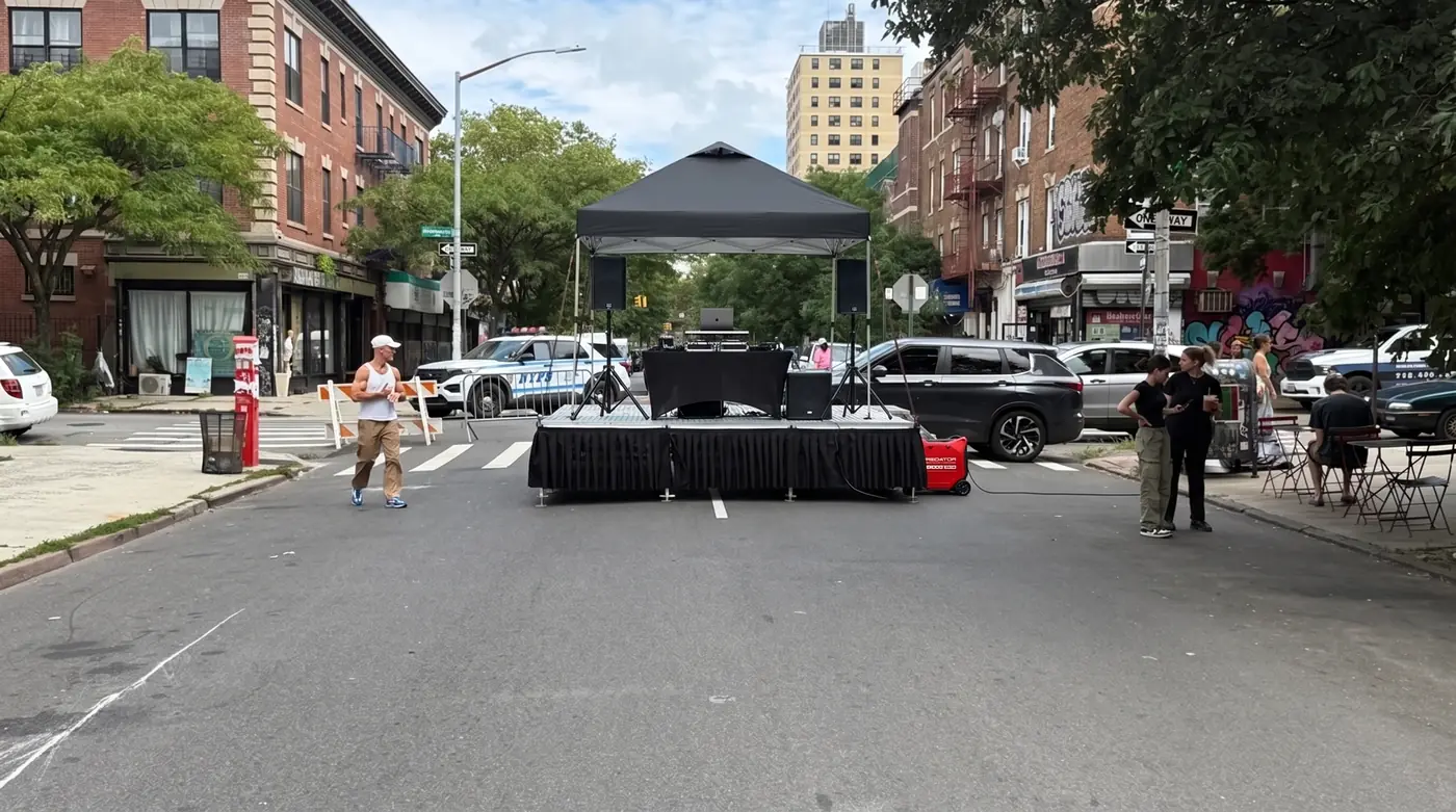 Portable stage with a DJ setup on a closed Bushwick street powered by a Predator 5000 generator set behind the stage
