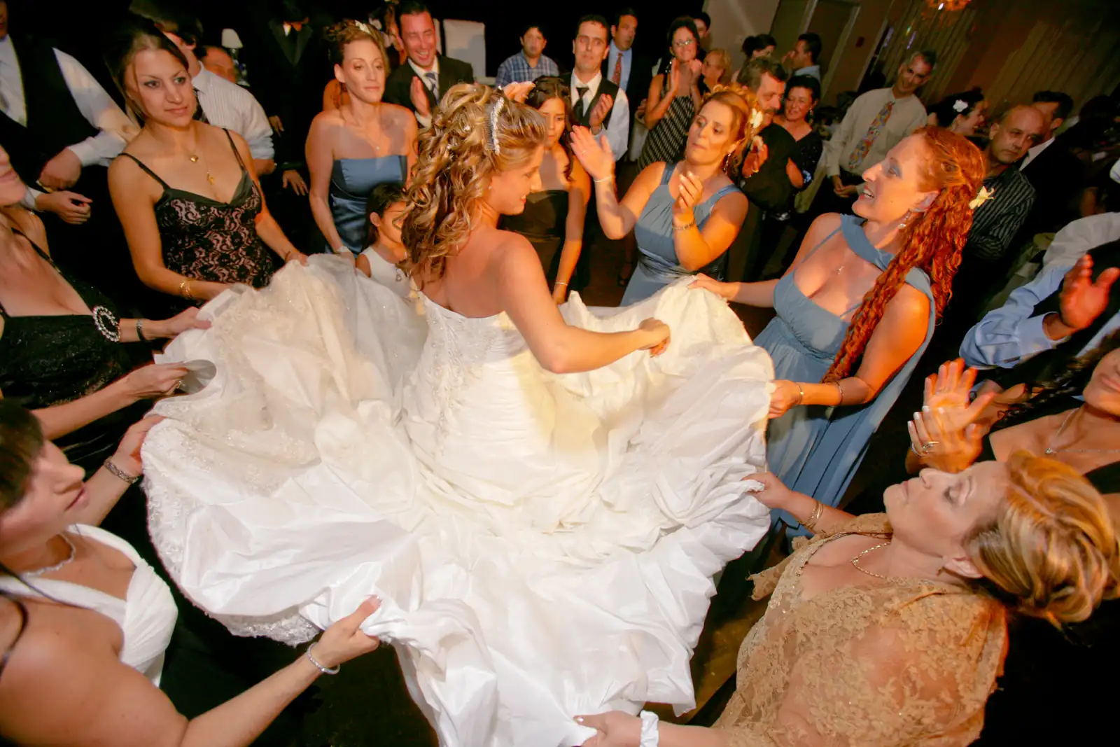 Bride spinning in her ball gown in the middle of a circle of guests clapping and dancing on a packed wedding dance floor