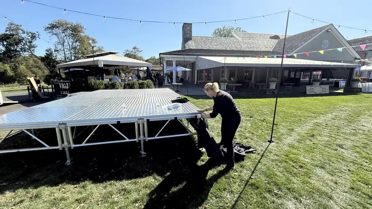 Our crew installing black stage skirting on an outdoor portable stage at a venue lawn