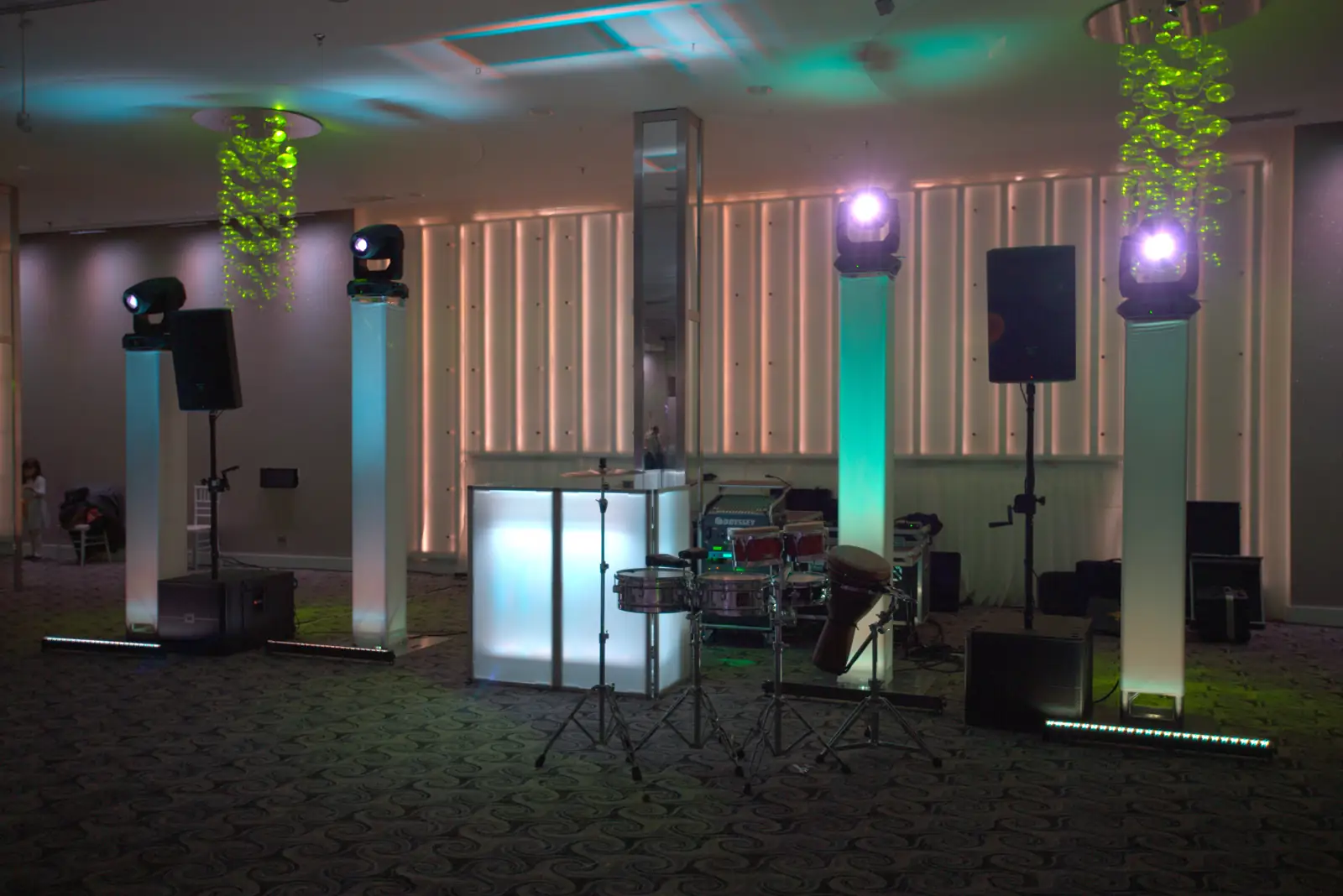 Event lighting with uplight towers, moving heads, a lit DJ booth and speakers in a venue
