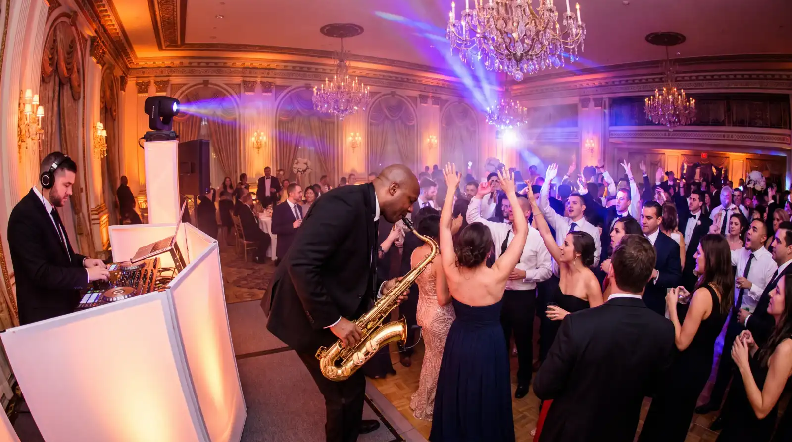 Saxophonist playing over the DJ on a packed wedding dance floor in a New York ballroom, guests dancing under moving head lights