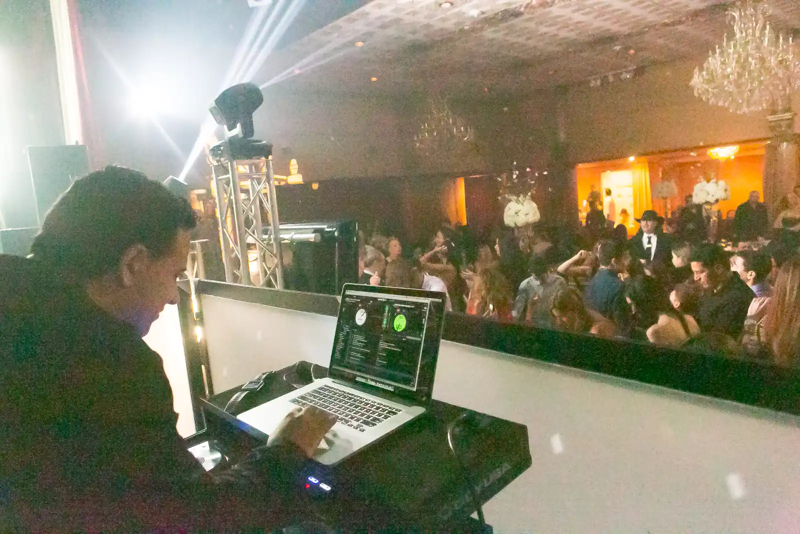 Our DJ mixing on a laptop with moving head lights over a packed mitzvah dance floor