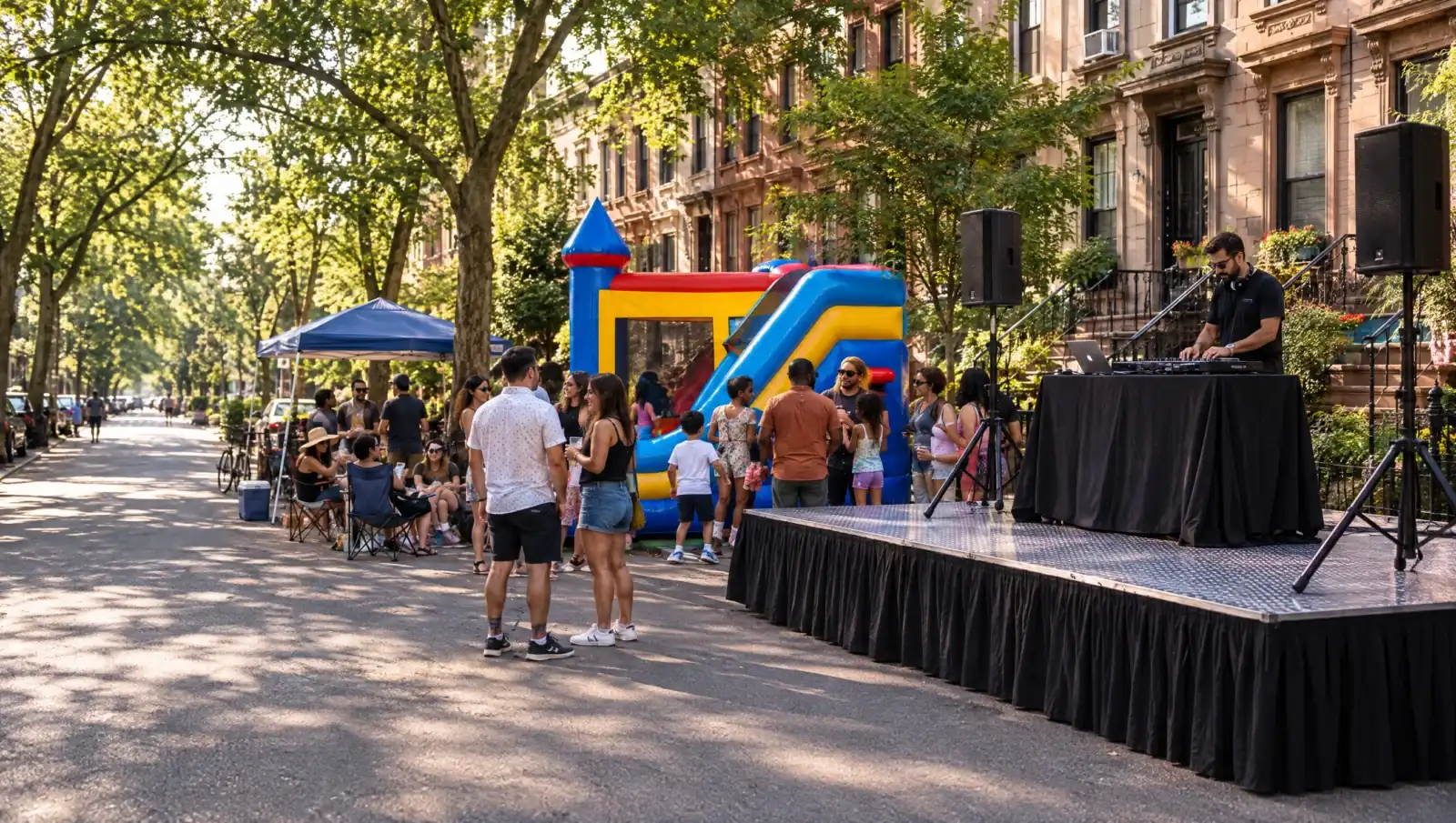 Party rentals Brooklyn NY: portable stage with a DJ and speakers next to a combo bounce house at a brownstone block party