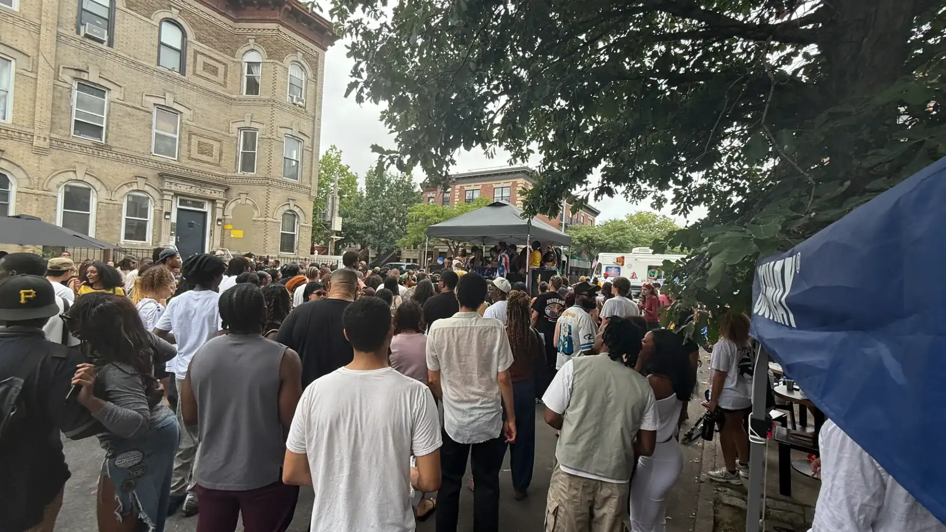 Party Rentals near Me: large crowd filling a Bushwick street facing a portable stage under a pop-up tent