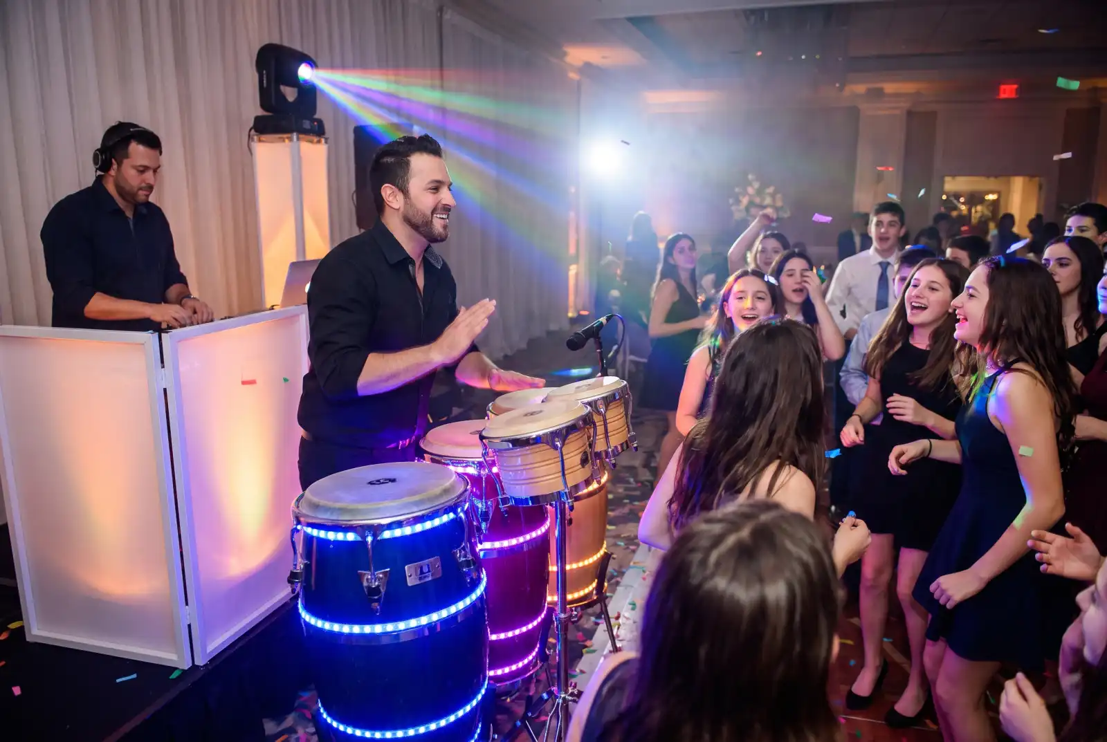 Percussionist on LED-lit congas and bongos next to the DJ booth as teens dance at a bar mitzvah