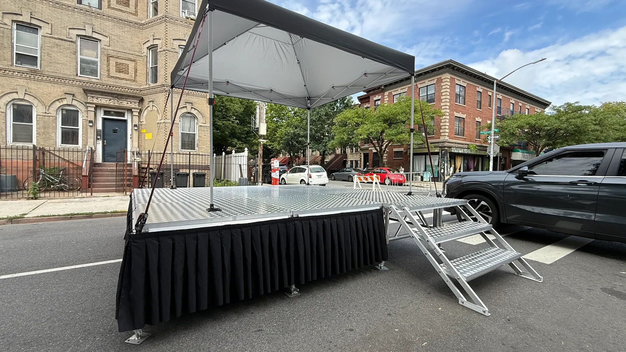 Side view of a portable stage with black skirting, a pop-up tent overhead and steps with handrails