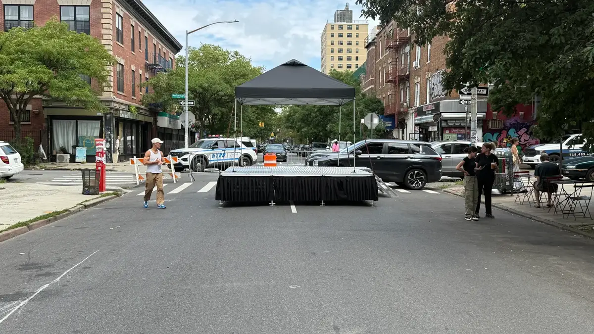 Portable stage under a tent in the middle of a closed Brooklyn street with barriers and a police car