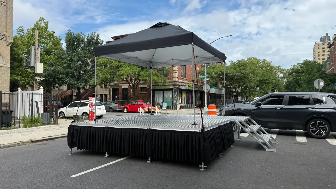 Portable stage with black skirting under a 10ft pop-up tent on a closed Brooklyn street with an access ramp