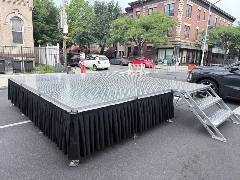 Portable stage with aluminum deck, black skirting and stage steps on a Bushwick street corner for a block party
