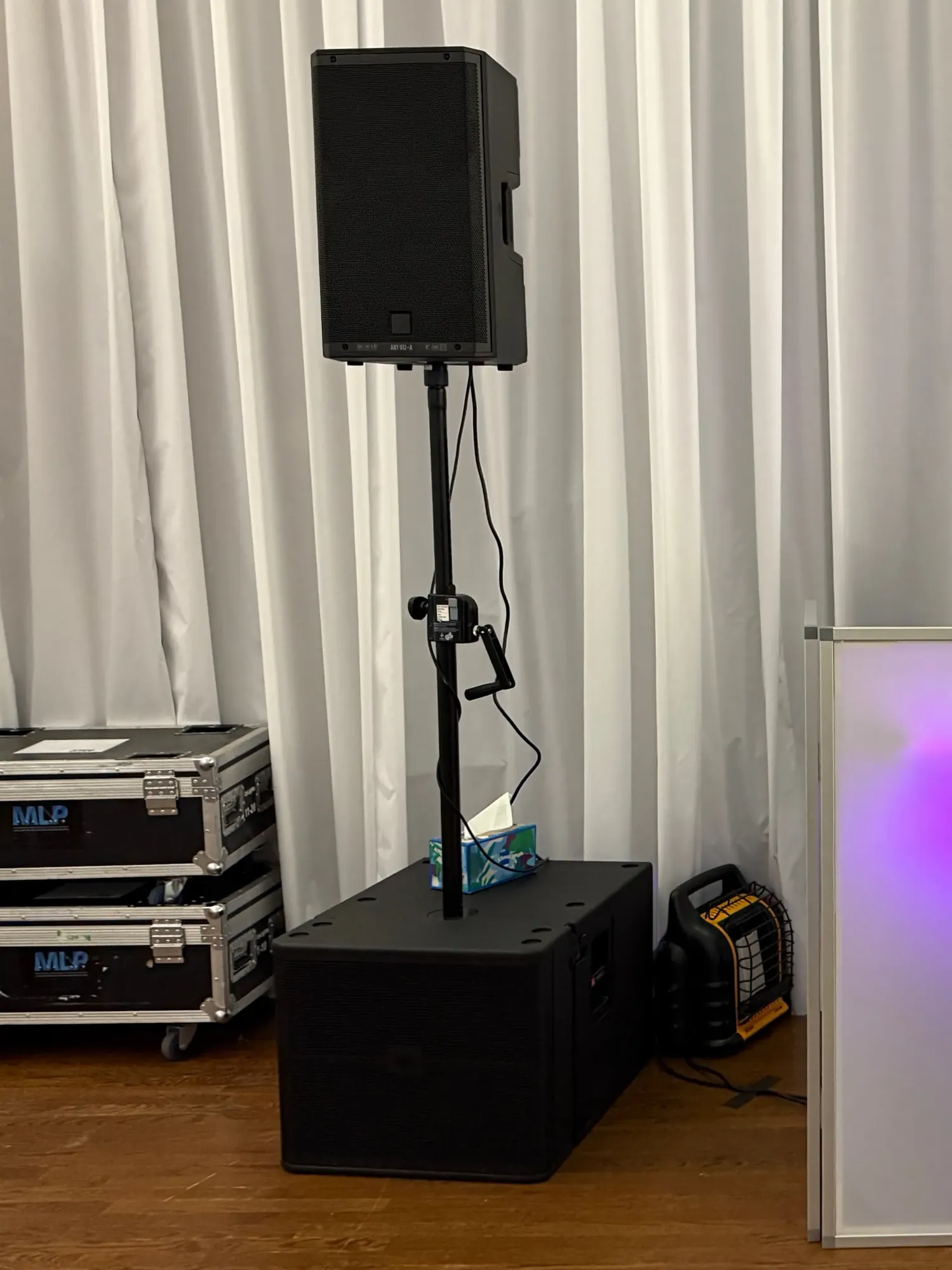Powered speaker on a tripod stand standing on a subwoofer against white draping at a wedding