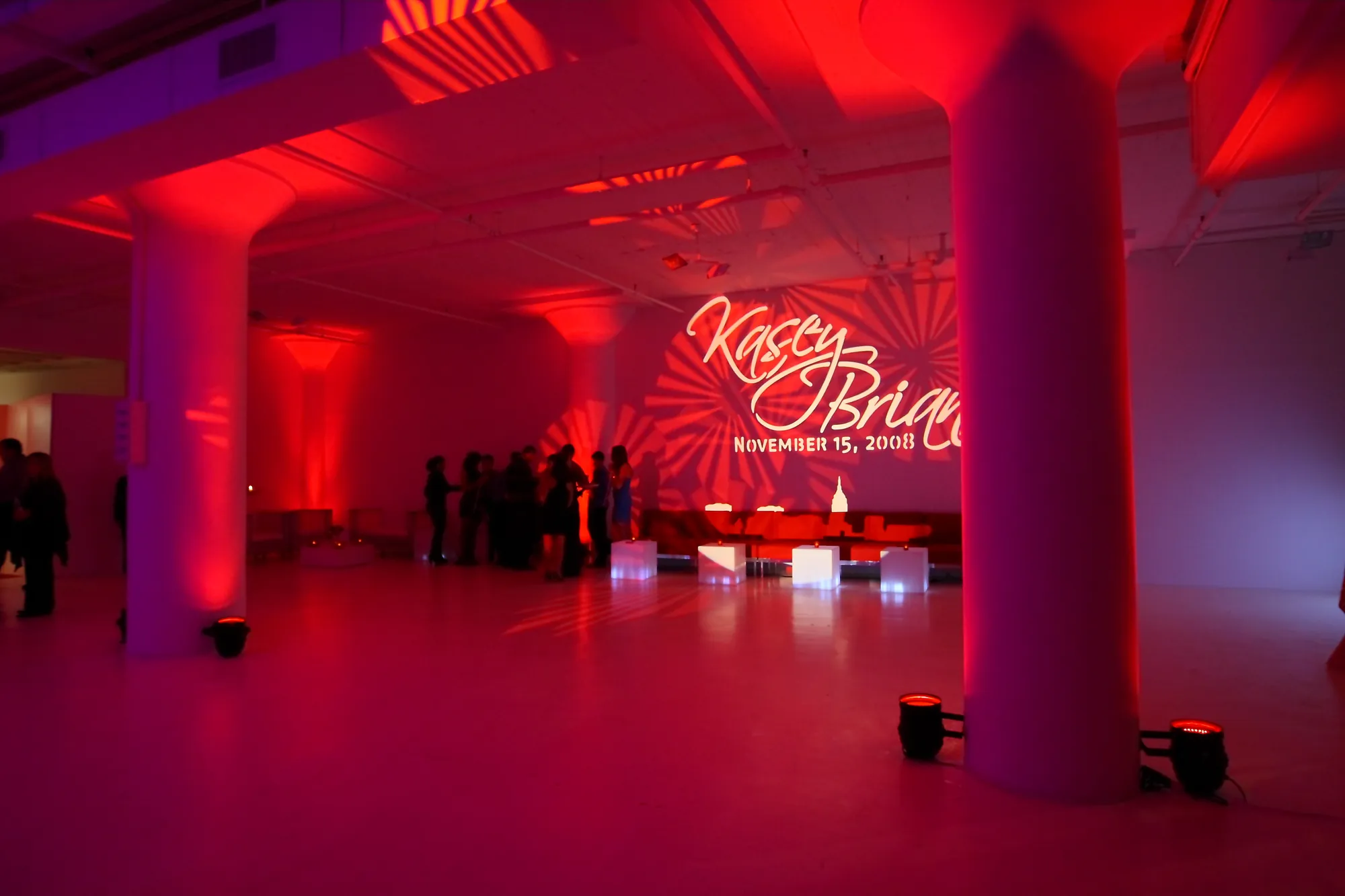 Sweet 16 venue lit with red uplighting on the columns and a custom monogram projected on the wall